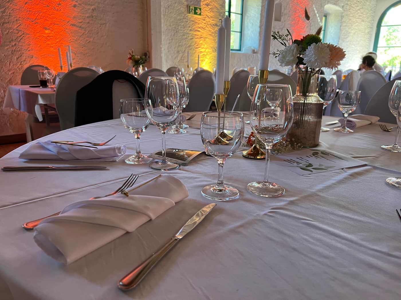 Festlich gedeckte Hochzeitstafel mit weißen Servietten, Kerzen und Blumen im Gewölbesaal