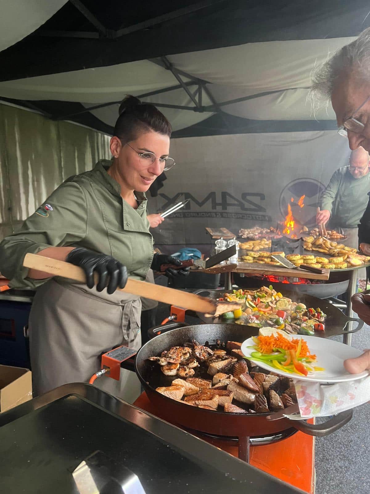 Köchin brät frischen Lachs und Garnelen am Cateringstand von Unter der Burg